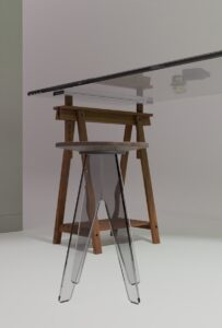 Clear glass table on wooden sawhorses with an acrylic stool.